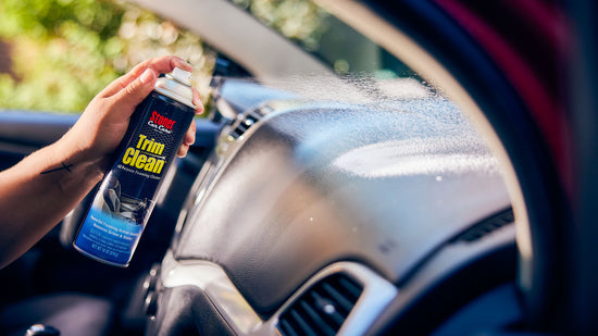 Person cleaning car interior trim with a spray bottle labeled 'Trim Clean'.