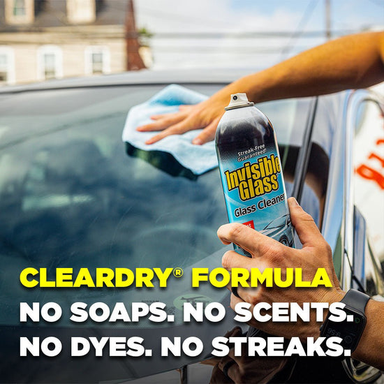 Person cleaning a car window with Invisible Glass glass cleaner, with text highlighting the clear dry formula.