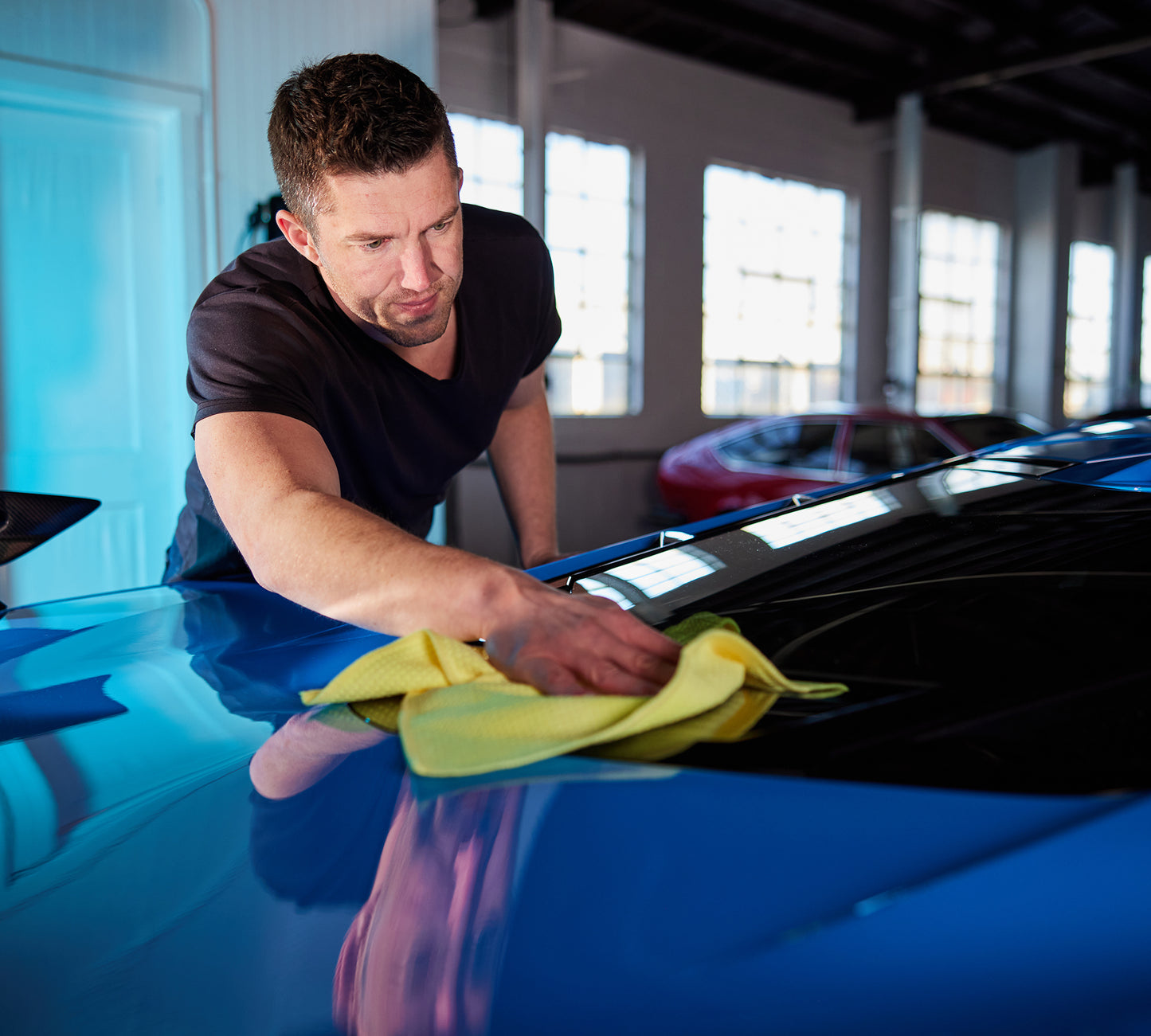 A man using the Premium Glass Microfiber – 16in X 16in - 370 GSM to clean the outside of a car
